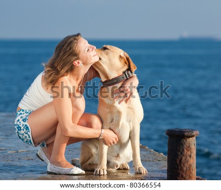 Young woman with Labrador male dog on the coast of the sea. Girl kissing her dog