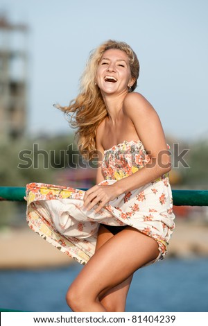 Blonde holds her skirt blown by wind. Girl laughing on open air