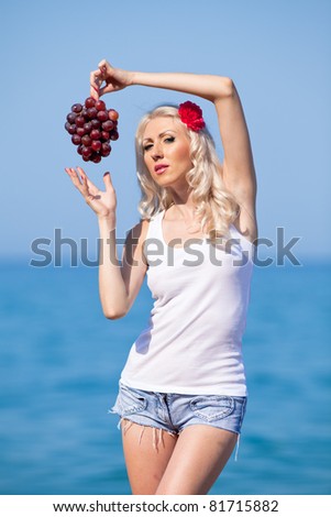 Attractive blonde at the sea. Girl with grapes on background of sea