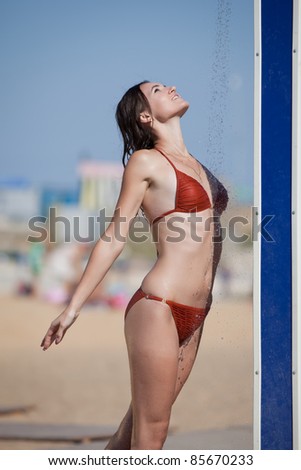 Wet girl in bikini on open air. Attractive young woman in orange swimwear takes shower on the beach