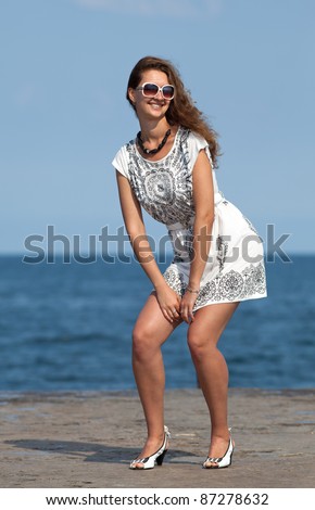 Attractive girl on pier. Young woman holds her skirt blown by wind