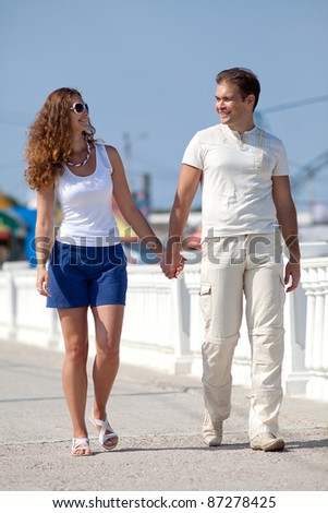 Attractive couple walking along pier. Young man and young woman on seashore