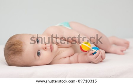 Charming baby. Baby girl with toy rattle lying on side looking at camera