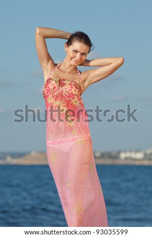 Girl at the sea. Attractive young woman is posing on background of sea. Lady in pink sarong looking at camera smiling