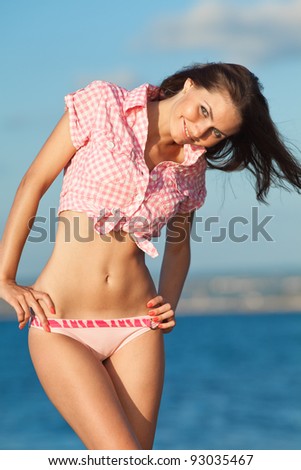 Girl at the sea. Attractive young woman is posing on background of sea. Lady in pink shirt on the beach
