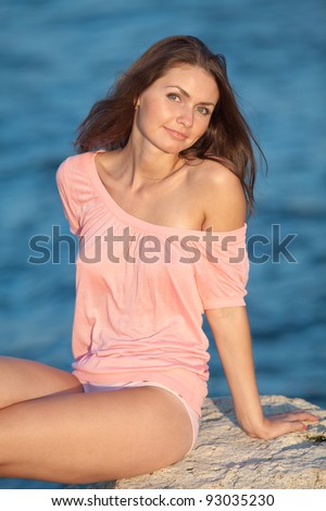 Girl at the sea. Attractive young woman in pink blouse sits on background of sea. Lady in  pink blouse looking at camera smiling