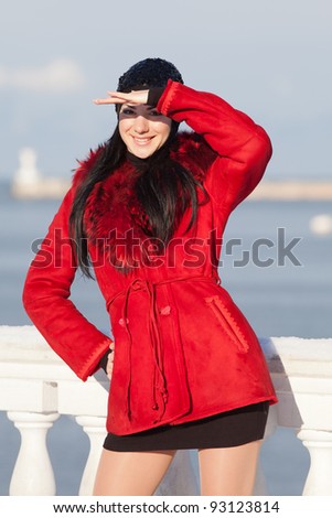 Beautiful young woman at winter. Attractive brunette in red looks, covering his eyes with his hand