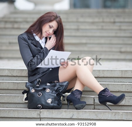 Attractive businesswoman on open air. Girl sitting on stairs talking on the phone