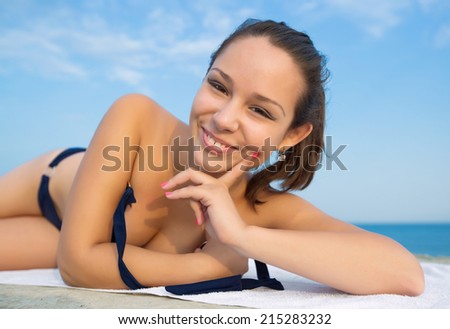 Girl lying down on open air. Young woman in dark swimwear lying on front looking at camera smiling