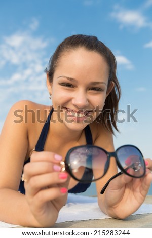 Girl lying down on open air. Young woman with sunglasses lying on front looking at camera smiling