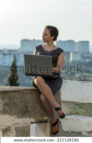 Young business woman outdoors. Girl with laptop sitting on concrete wall looking away