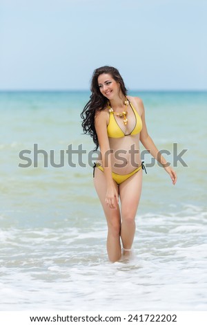 Expectant mother emerging from the sea. Pregnant woman in yellow bikini on the beach