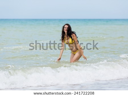 Expectant mother playing in the sea. Pregnant woman in yellow bikini on the beach
