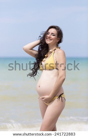 Expectant mother at the sea. Pregnant woman in yellow bikini posing on the beach