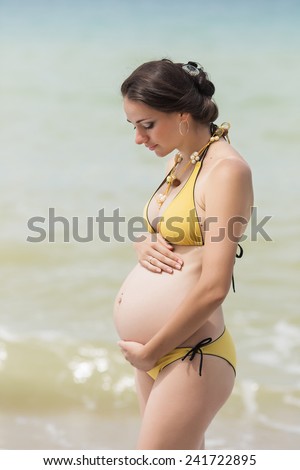 Expectant mother on the beach. Pregnant woman in yellow bikini at the sea
