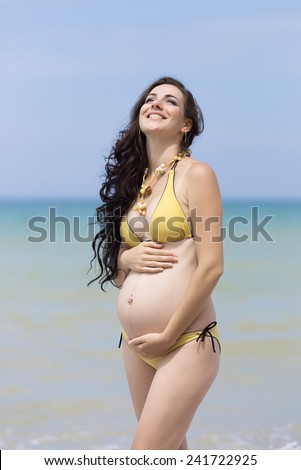 Expectant mother at the sea. Pregnant woman in yellow bikini posing on the beach
