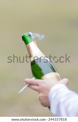 Hand holding champagne bottle and cigarette. Smoke after opening champagne bottle