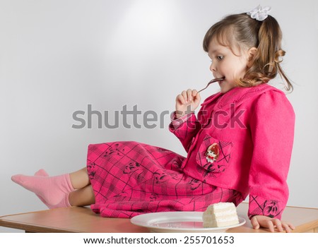 Charming preschooler in pink sits on table and eats cake. Little girl eating dessert