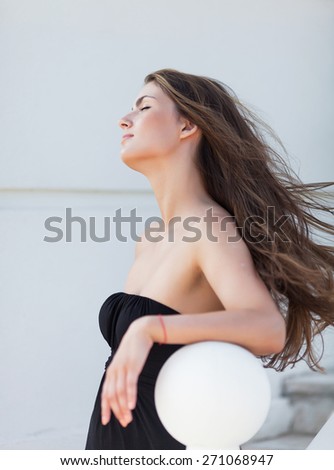Portrait of girl in the park. Bareheaded young woman in black sleeveless dress posing on open air with eyes closed