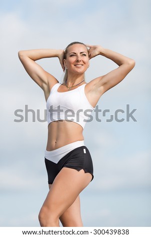 Female doing exercises on open air. Middle age woman stands with arms raised outdoors