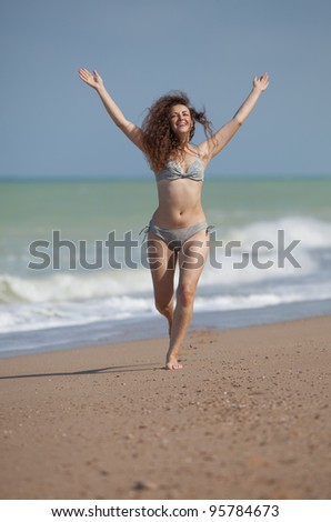 Girl runs with arms raised. Attractive young woman runs along the beach