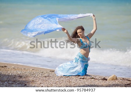 Brunette in costume for belly-dance is dancing on the beach. Girl is dancing outdoors
