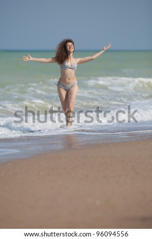 Girl runs with arms raised. Attractive young woman runs along the beach