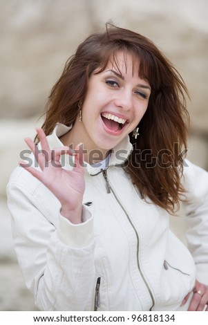 Attractive dark-haired young woman winking showing Ok looking at camera laughing