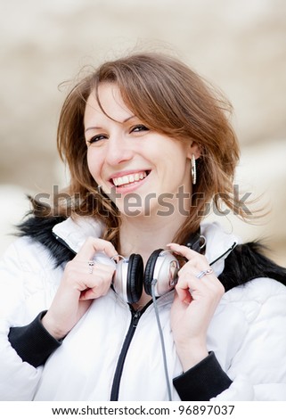 Monochrome dressed girl with headphones on open air. Attractive dark haired woman with headphones looking at camera smiling