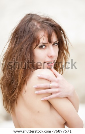 Topless young woman on open air. Attractive dark haired woman hiding her naked chests under her arms. She looking at camera smiling