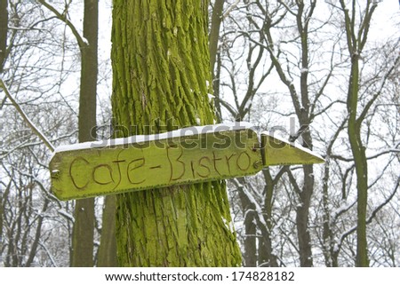 Cafe-bistro sign showing direction and carved in wood covered in lichen.
