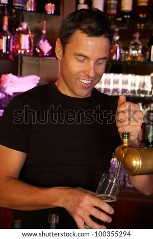 Portrait Of Barman Standing Behind Bar Pouring Beer