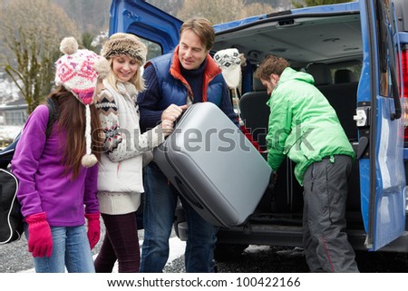 Family Unloading Luggage From Transfer Van Outside Chalet On Ski Holiday