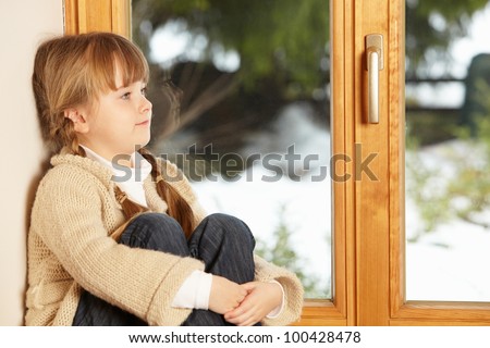 Young Girl Sitting On Window Ledge Looking At Snowy View