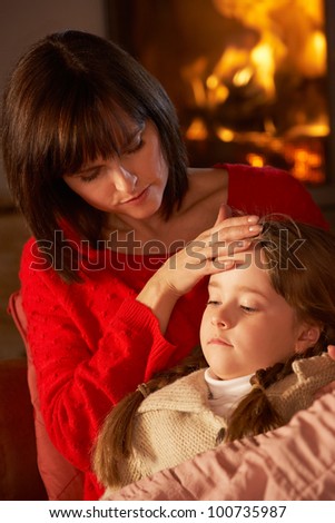 Mother Comforting Sick Daughter On Sofa By Cosy Log Fire