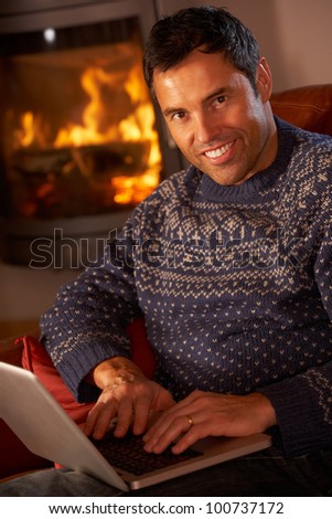 Middle Aged Man Using Laptop Computer By Cosy Log Fire