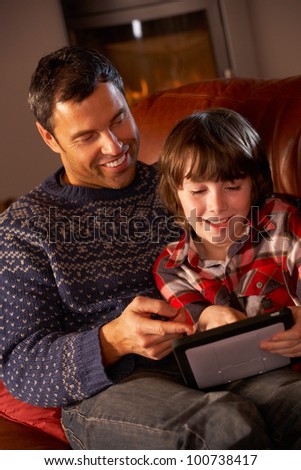 Father And Son Using Tablet Computer By Cosy Log Fire