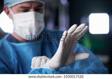 Male surgeon putting on latex gloves in preparation
