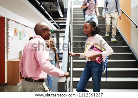 Female High School Student Talking With Teacher In Busy Corridor