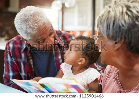 Grandparents Reading Book With Baby Granddaughter At Home