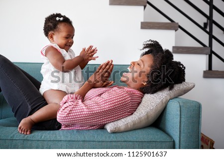 Mother Lying On Sofa At Home Playing Clapping Game With Baby Daughter