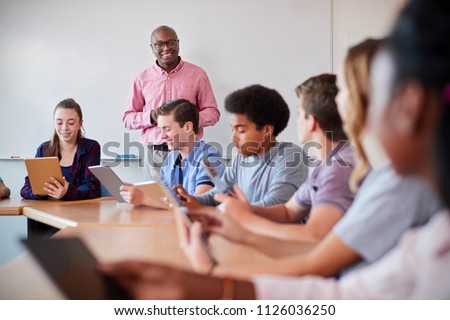 High School Teacher With Pupils Using Digital Tablets In Technology Class