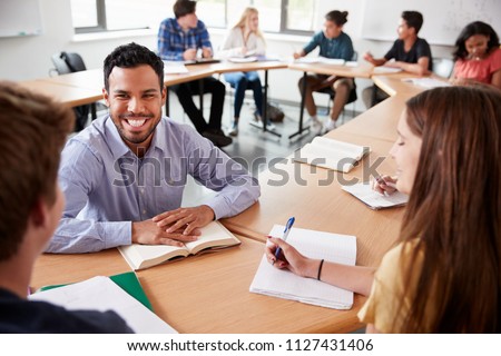 Male High School Tutor With Pupils Sitting At Table Teaching Maths Class
