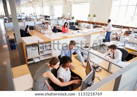 Colleagues working at a womanâ€™s workstation in a busy office