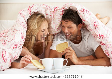 Couple Snuggled Under Duvet Eating Breakfast