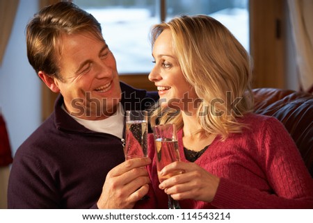 Middle Aged Couple Sitting On Sofa With Glasses Of Champagne