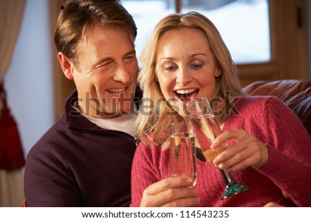 Middle Aged Couple Sitting On Sofa With Glasses Of Champagne
