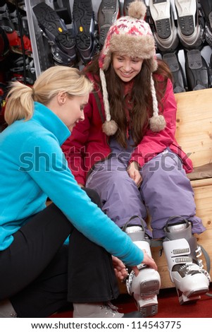 Sales Assistant Helping Teenage Girl To Try On Ski Boots In Hire Shop