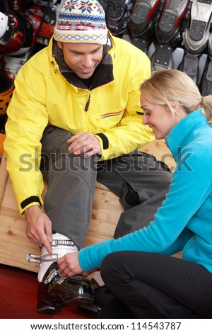Sales Assistant Helping Man To Try On Ski Boots In Hire Shop