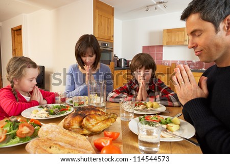Family Saying Grace Before Eating Lunch Together In Kitchen